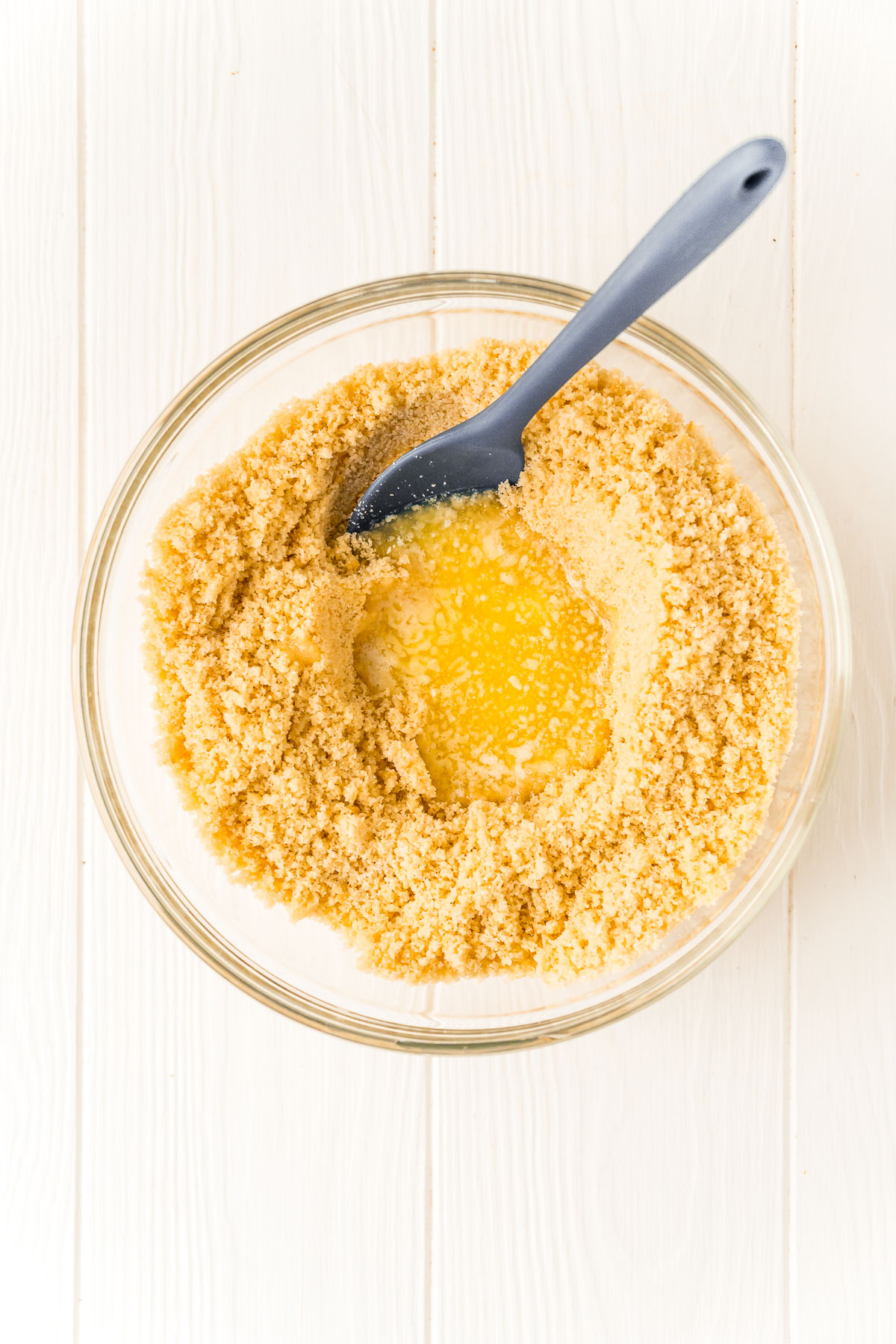 Cookie crumbs in a bowl with melted butter and a mixing spoon.