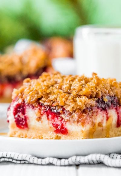 Close up photo of a slice of cranberry cheesecake bars on a small white plate.