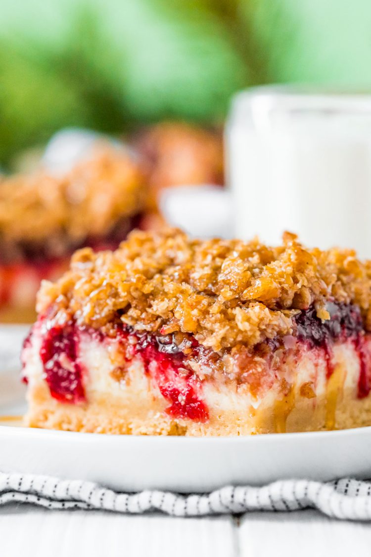 Close up photo of a slice of cranberry cheesecake bars on a small white plate. 