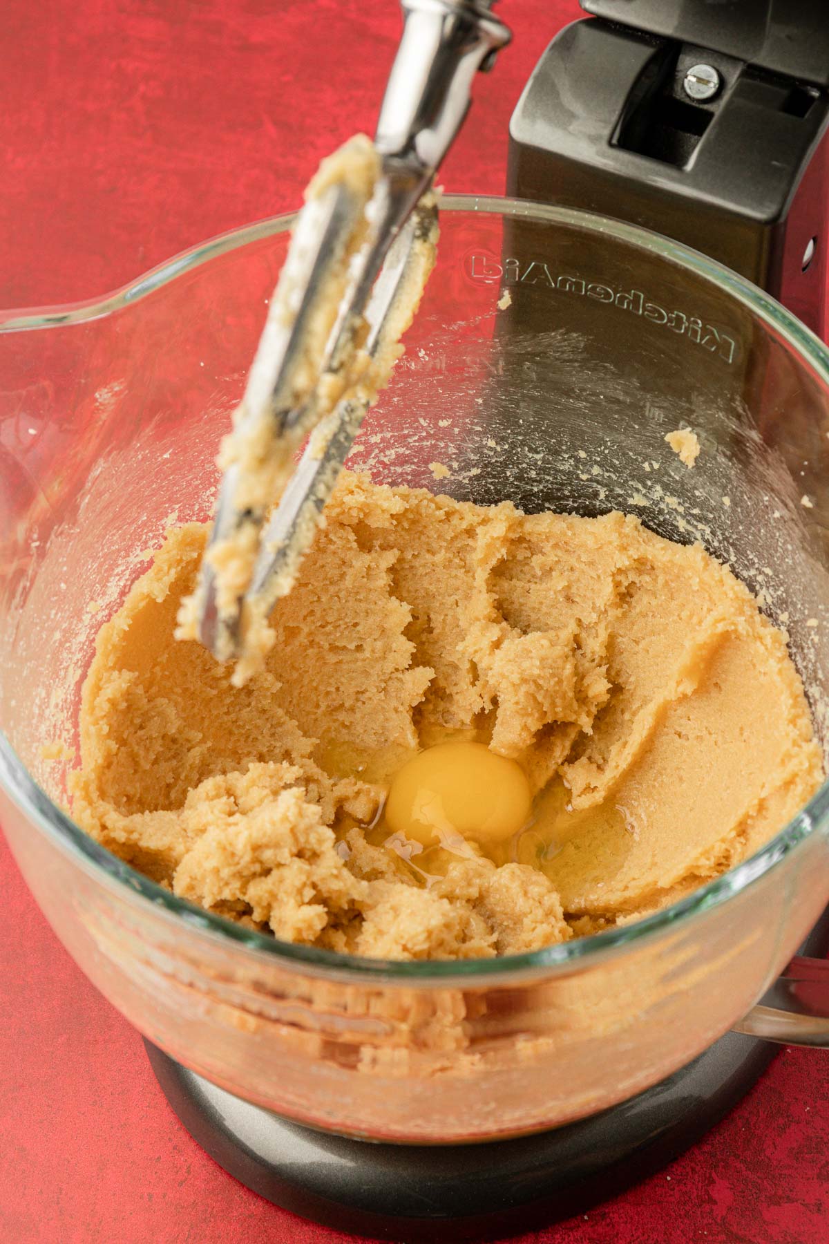 Eggs being added to a glass mixing bowl with butter and sugar to make cookie dough.