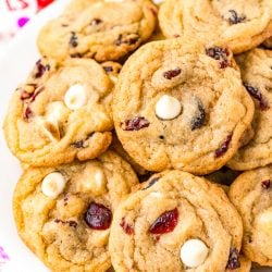 A white plate filled with cookies with white chocolate chips and craisins.