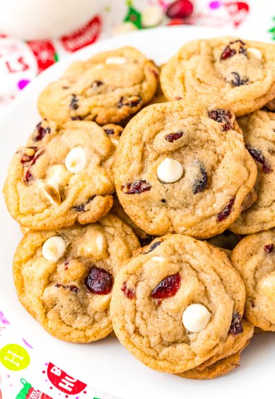 A white plate filled with cookies with white chocolate chips and craisins.
