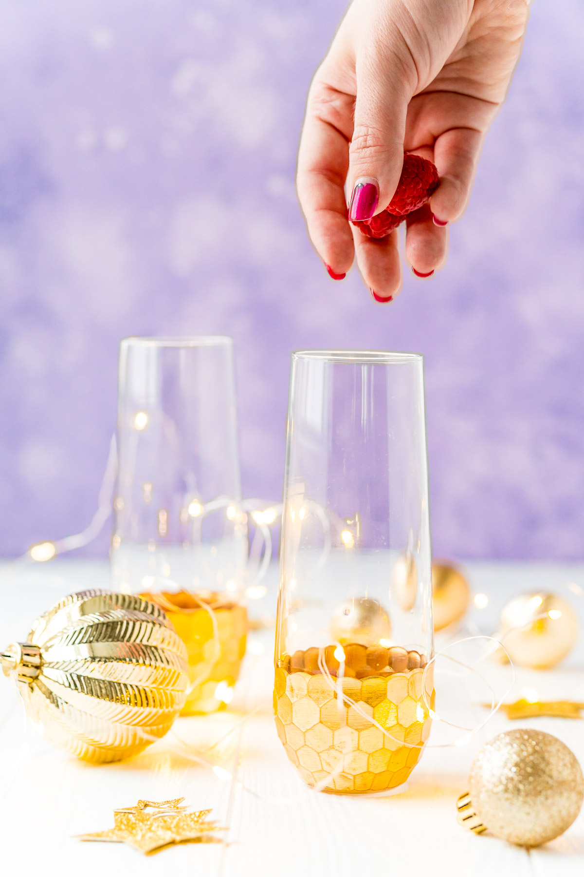 Woman's hand dropping fresh raspberries into a champagne flute to make a cocktail.