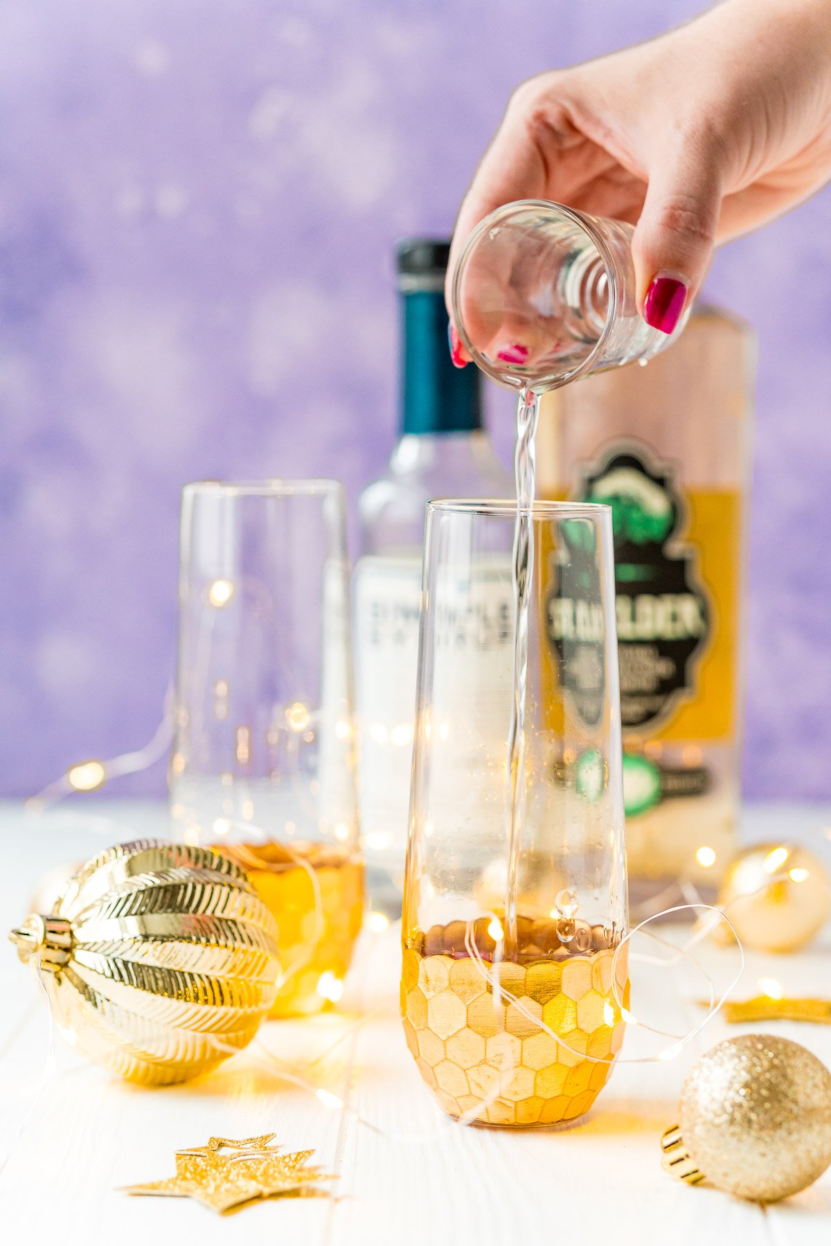 Woman's hand pouring liquor into a champagne flute.