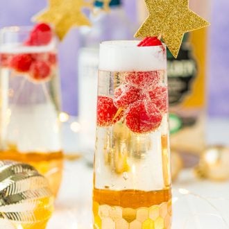 Close up photo of a champagne flute filled with a cocktail and raspberries.