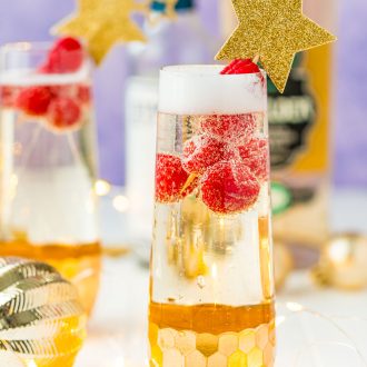 Close up photo of a champagne flute filled with a cocktail and raspberries.