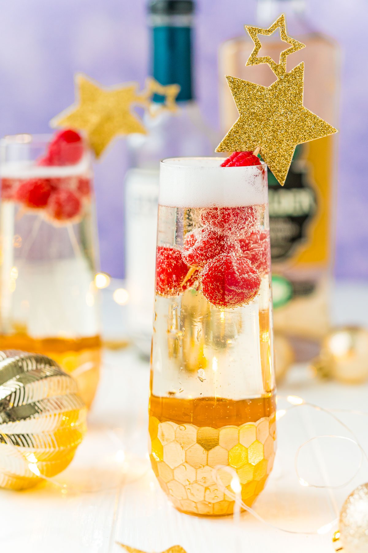 Close up photo of a champagne flute filled with a cocktail and raspberries.