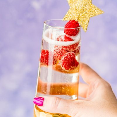 Woman's hand holding up a champagne cocktail with raspberry garnish.
