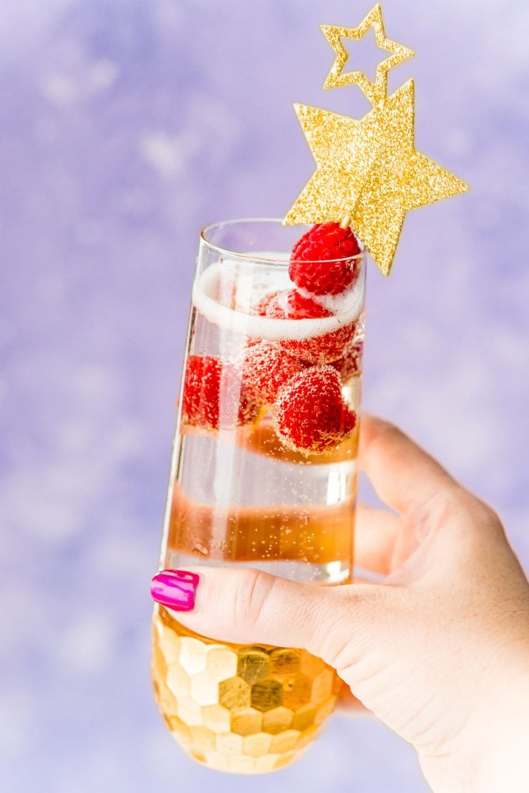 Woman's hand holding up a champagne cocktail with raspberry garnish.