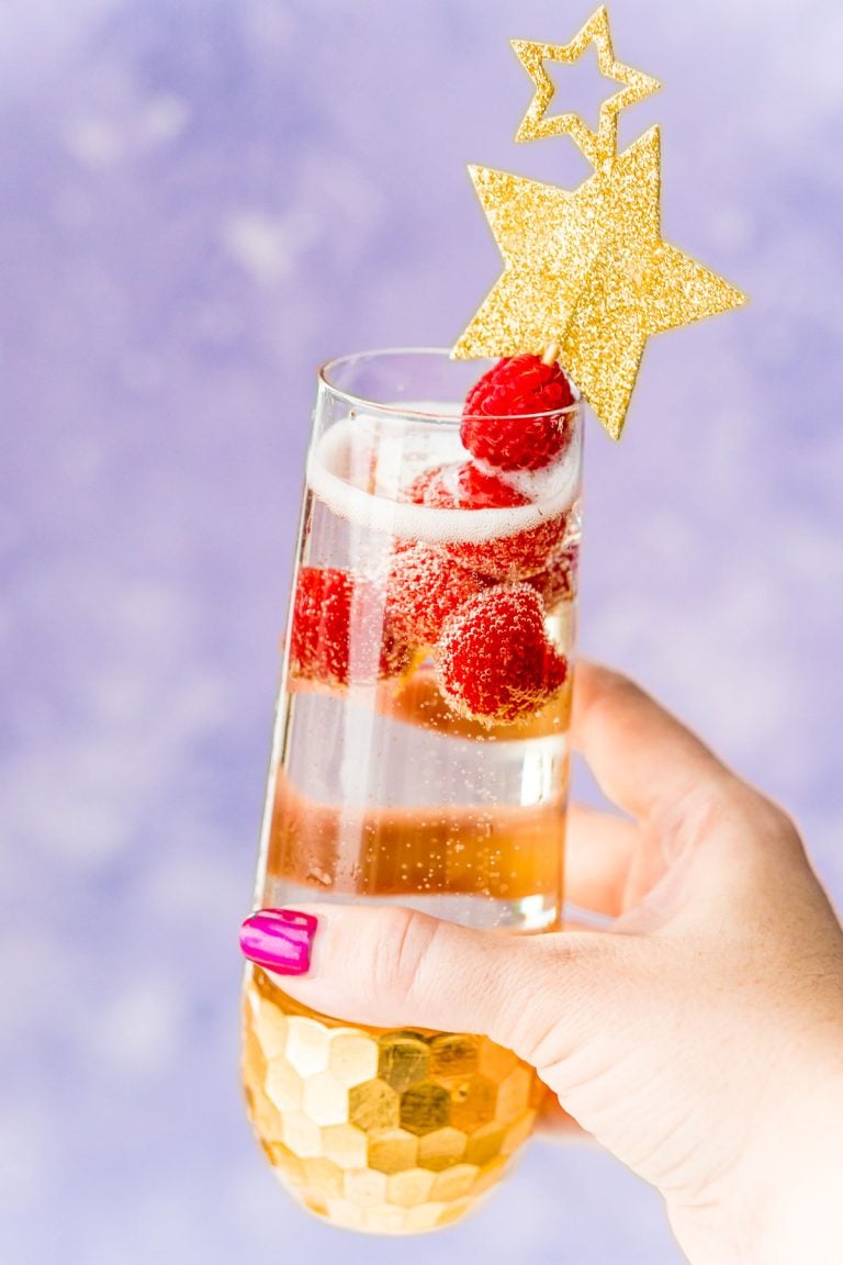 Woman's hand holding up a champagne cocktail with raspberry garnish.