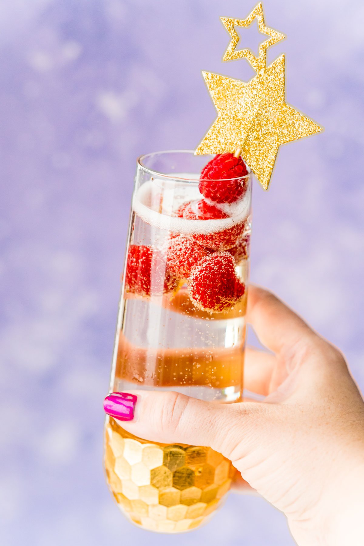 Woman's hand holding up a champagne cocktail with raspberry garnish.