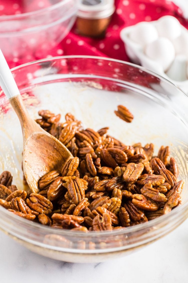 pecans in a mixing bowl with a wooden spoon.