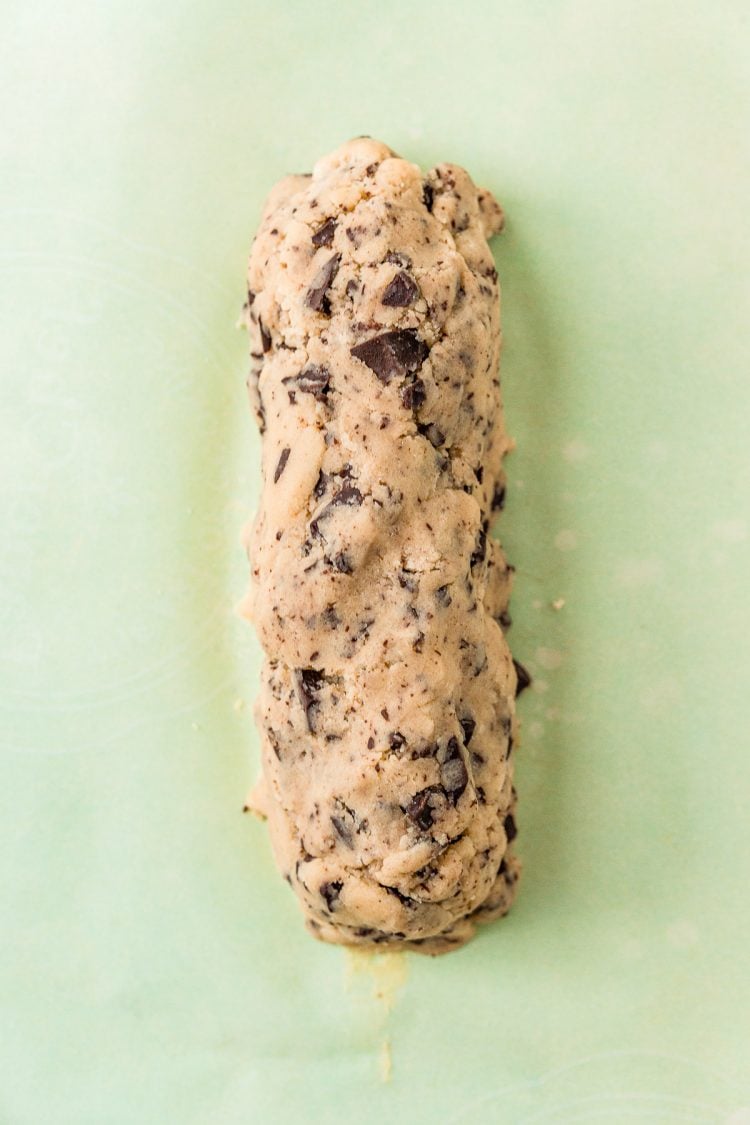 Chocolate chunk cookie dough formed into a log on parchment paper.