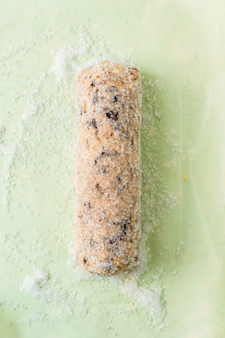Log of cookie dough rolled in coarse sugar on parchment paper.