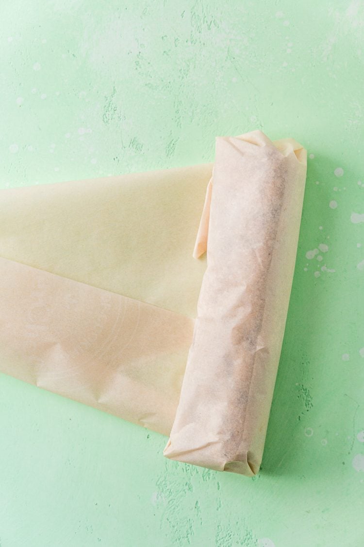 Cookie dough being rolled up in parchment paper.