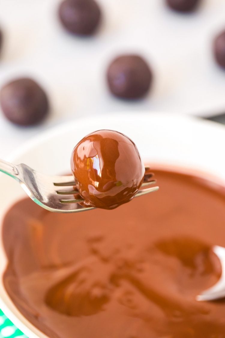 A fork with a truffle on it that has been dipped in melted chocolate.