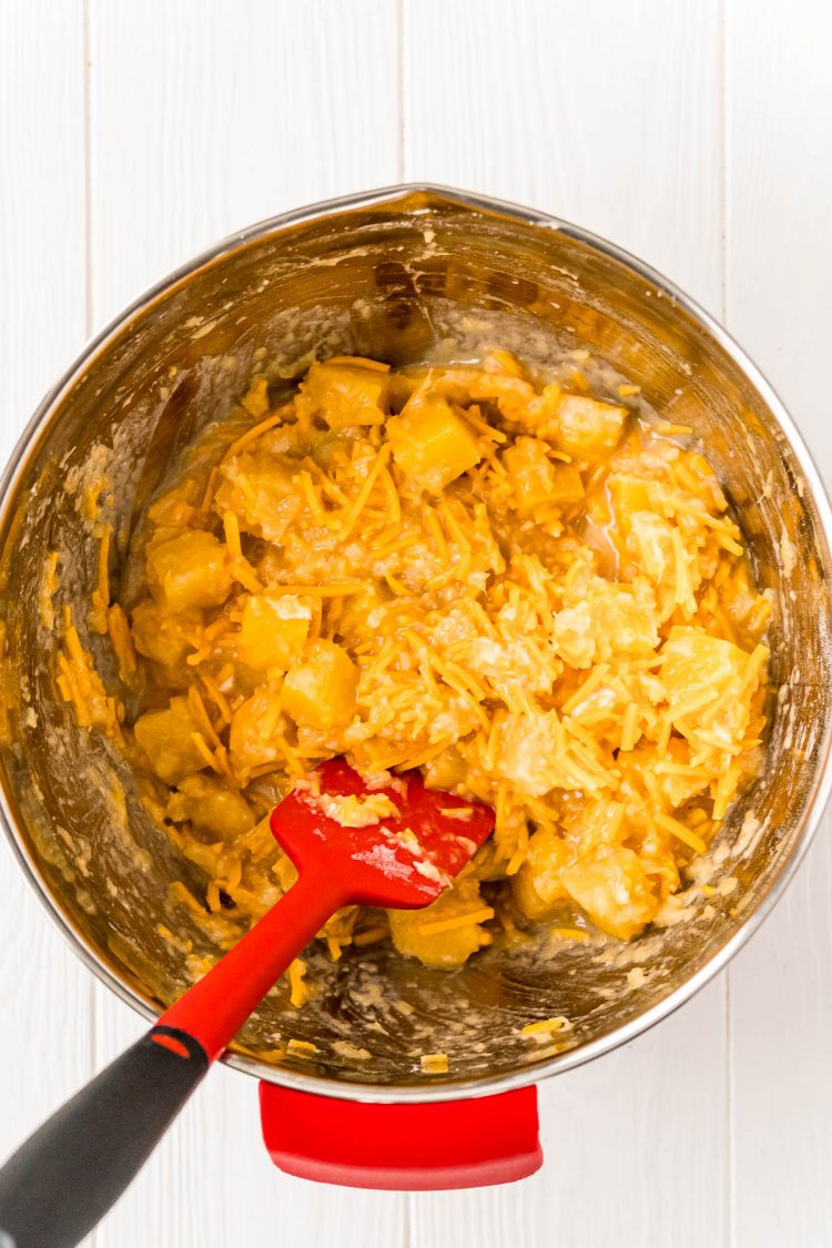 casserole filling being mixed in a metal bowl with a rubber spatula.