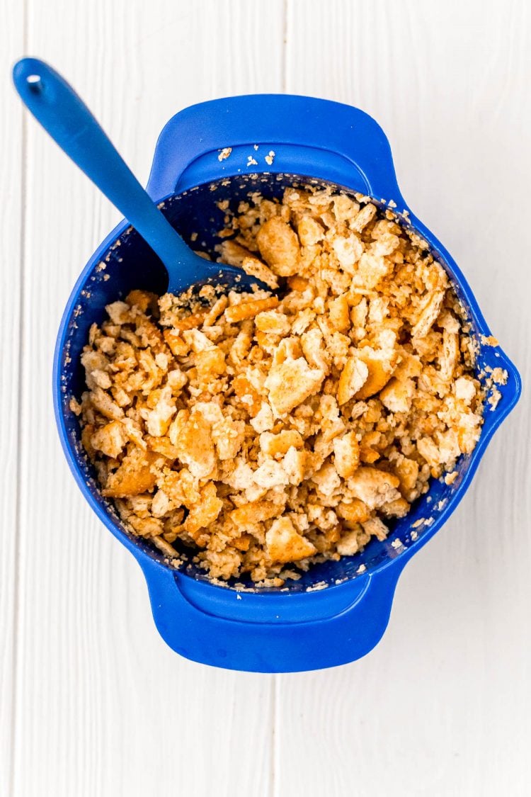 Crushed crackers and butter being mixed in a blue bowl.