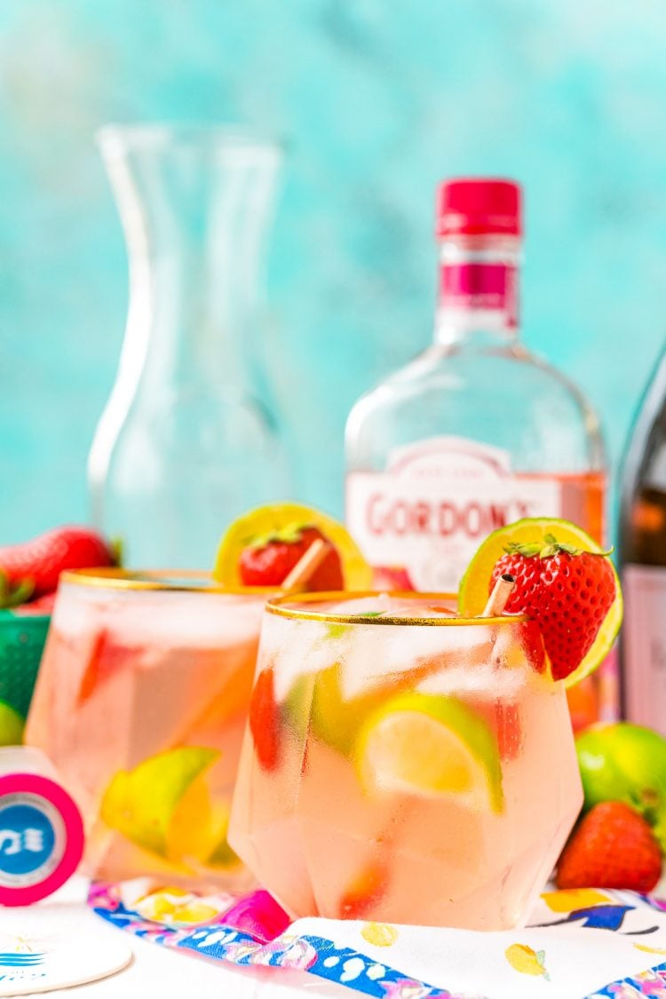 Glasses with a pink cocktail in them next to bottles of liquor on a table. 