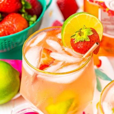Close up photo of a pink gin spritz in a gold rimmed glass garnished with a lime and strawberry.