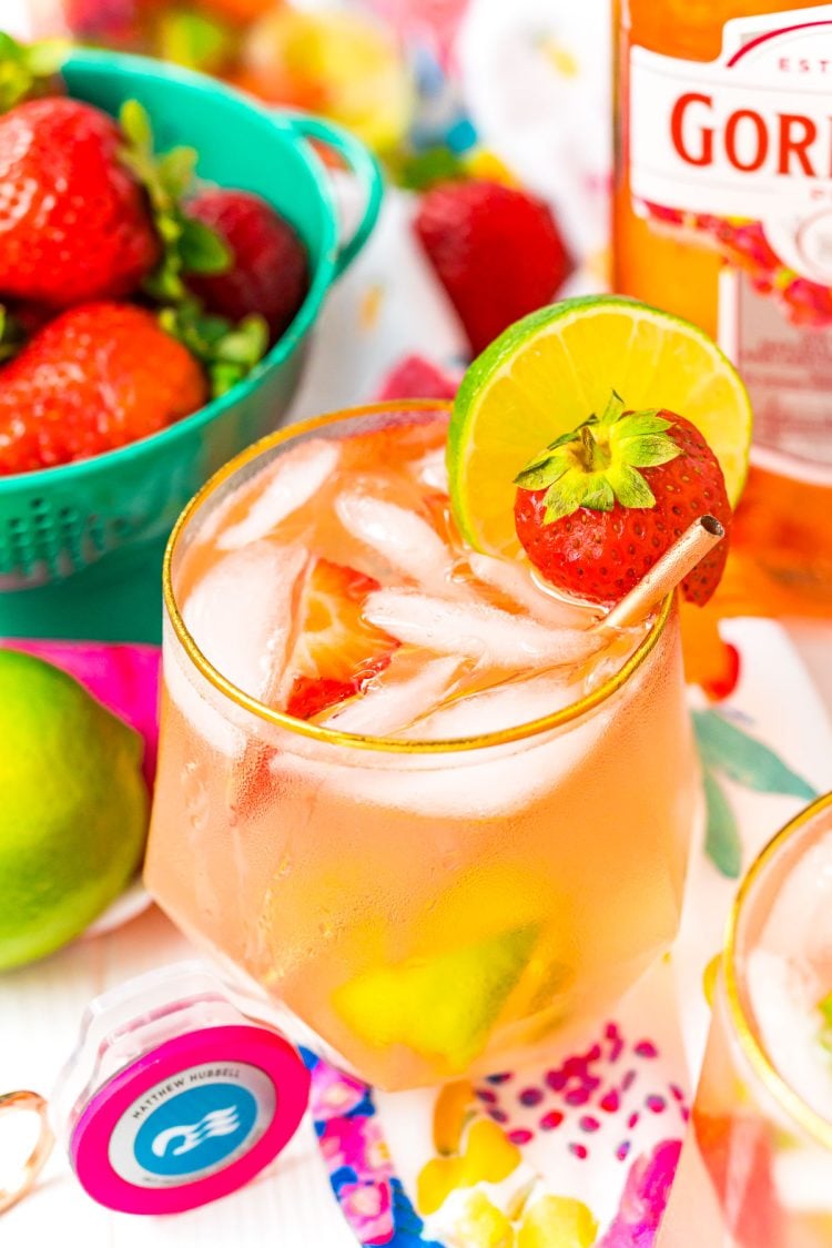 Close up photo of a pink gin spritz in a gold rimmed glass garnished with a lime and strawberry.