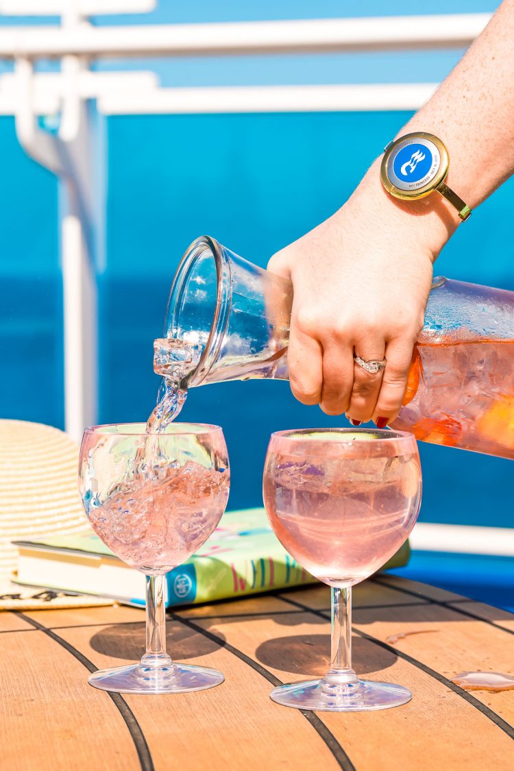 Woman pouring a cocktail out of a carafe into wine glasses on the deck of a cruise ship.