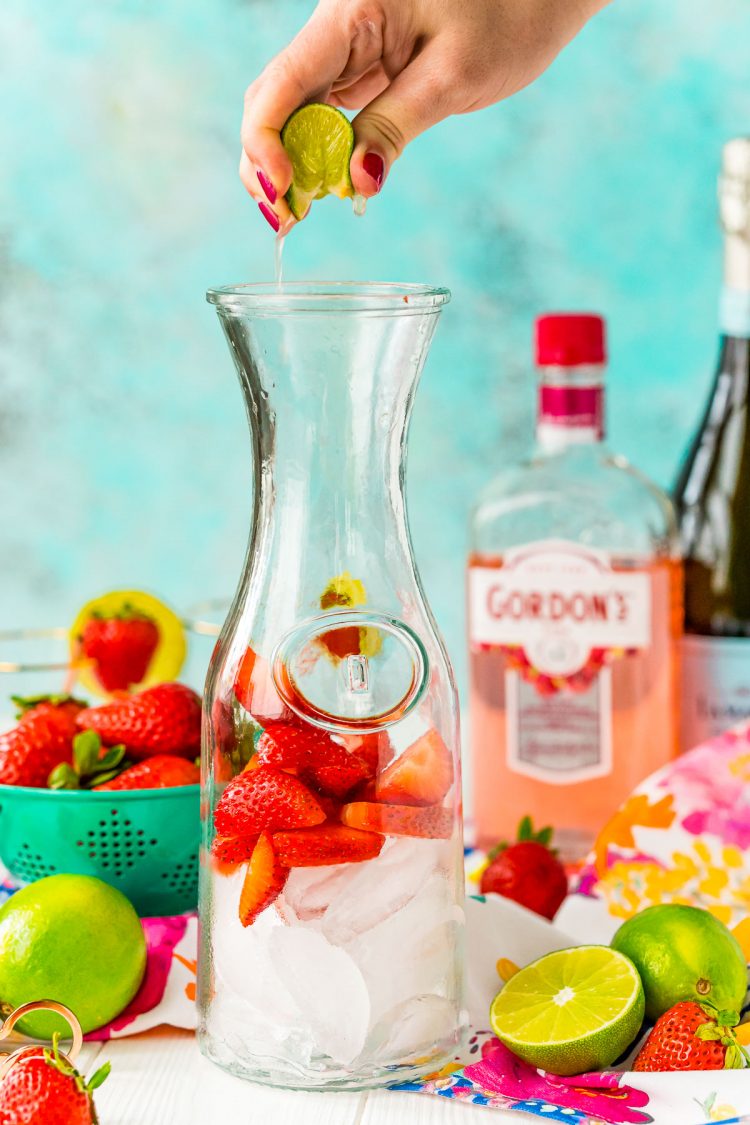 Woman's hand squeezing lime juice into a carafe with strawberries and ice.