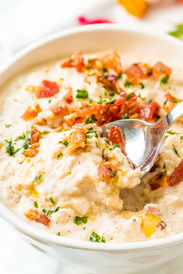 Spoon taking a scoop out of a bowl of cauliflower chowder.