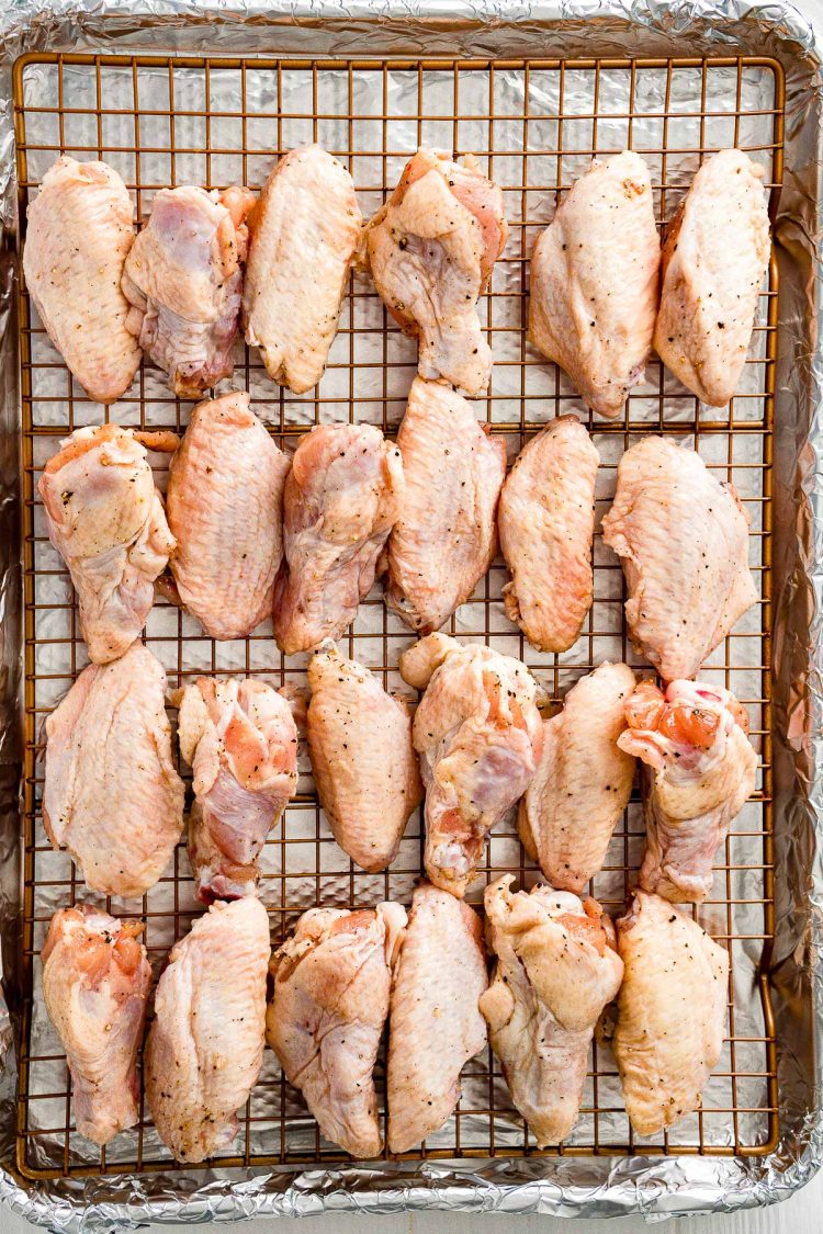 Uncooked chicken wings arranged on a wire rack on a baking sheet.