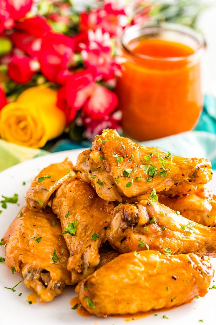 Chicken wings on a white plate with buffalo sauce in the background.