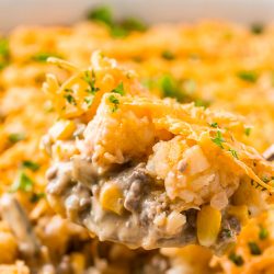 Close up photo of a serving spoon scooping tater tot hotdish out of a casserole dish.