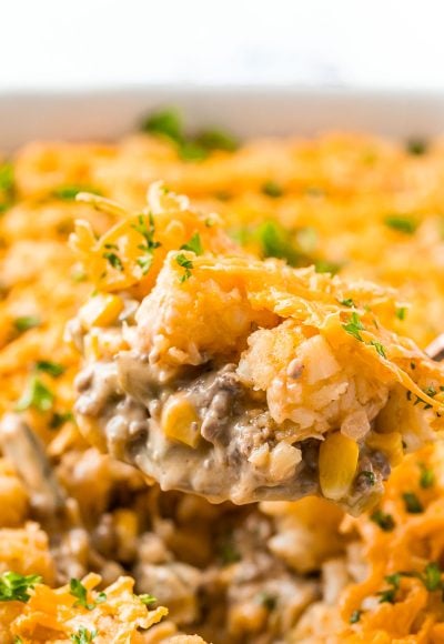 Close up photo of a serving spoon scooping tater tot hotdish out of a casserole dish.