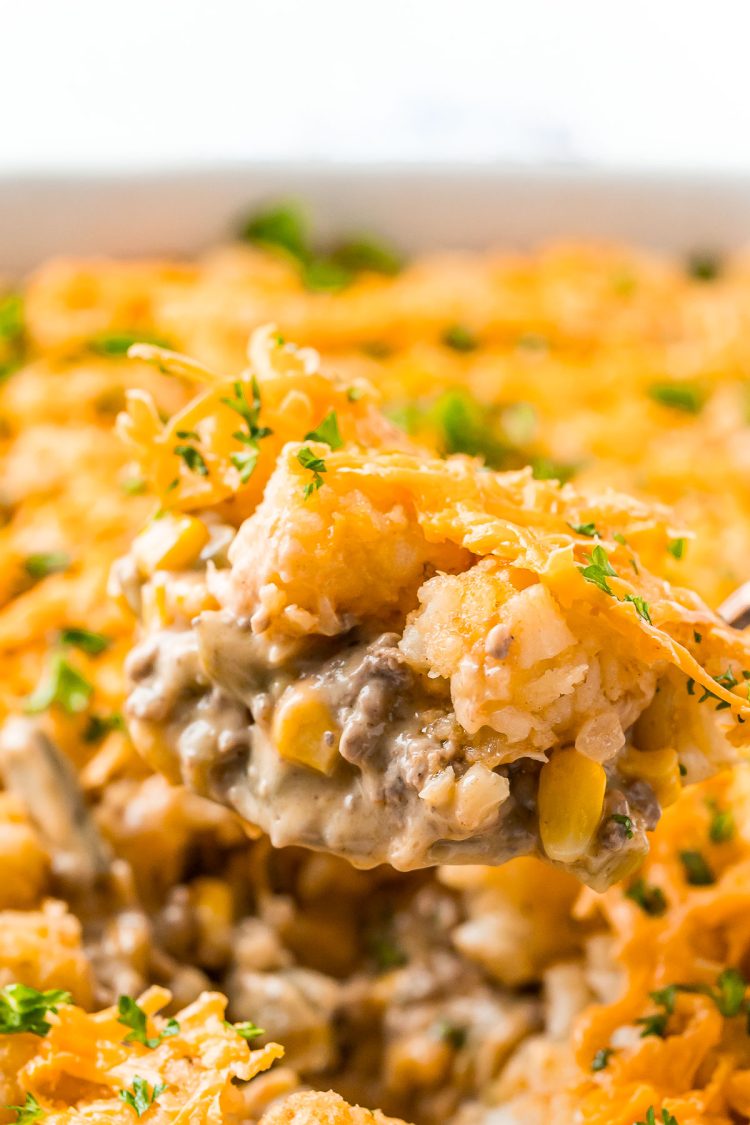 Close up photo of a serving spoon scooping tater tot hotdish out of a casserole dish.