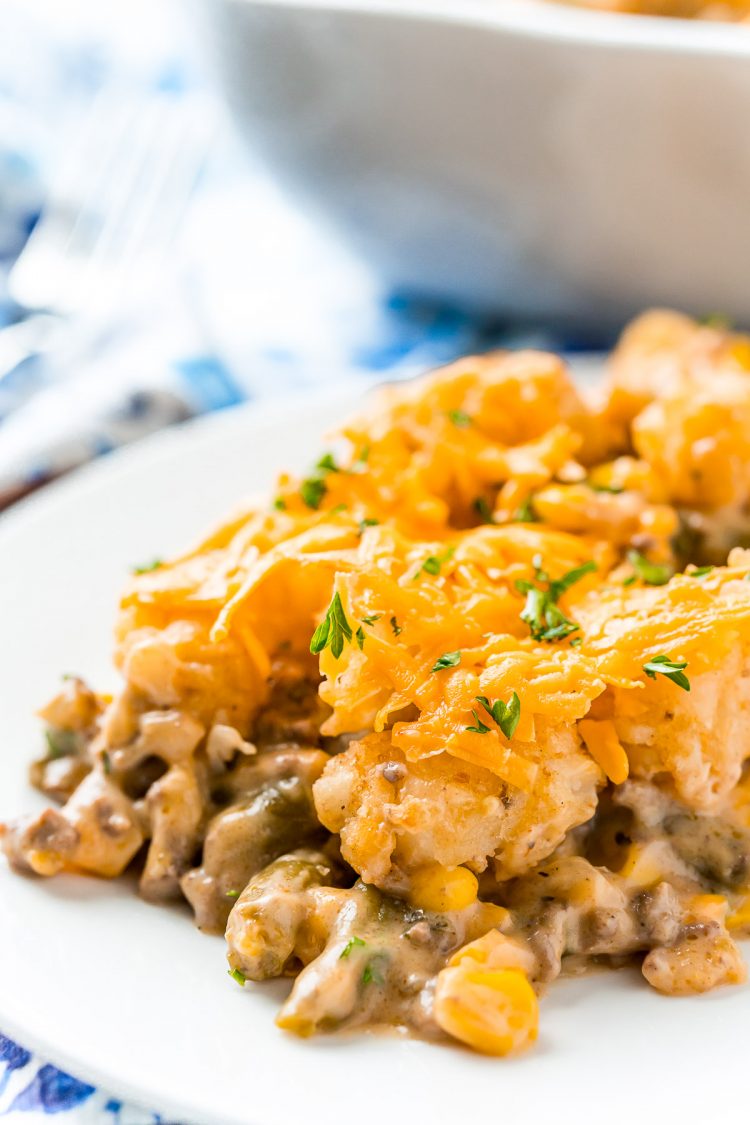 A scoop of tater tot casserole on a white plate on a blue napkin.