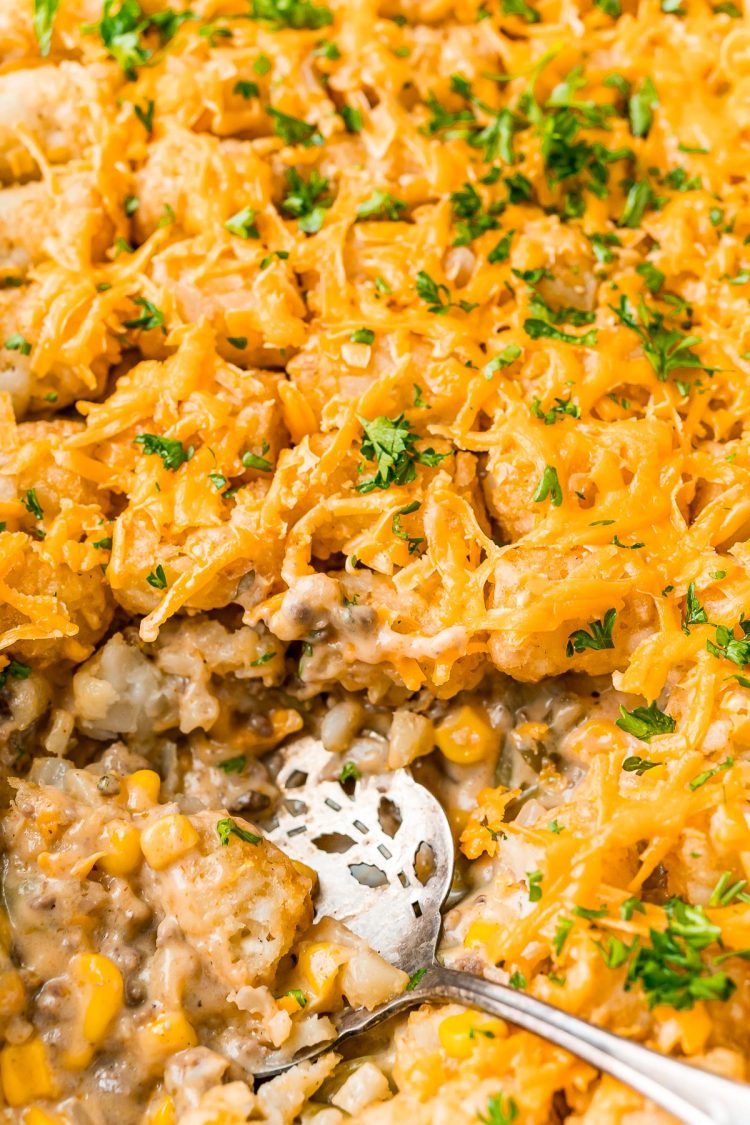 Close up overhead photo of a tater tot hot dish with a serving spoon resting in it.