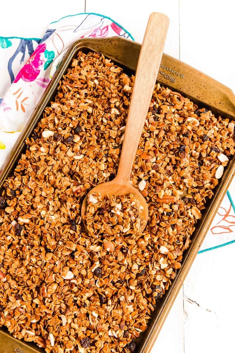 Homemade granola on a sheet pan with a wooden spoon scooping it.