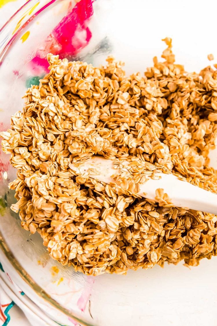 Oats being mixed with melted butter and spices in a glass bowl.