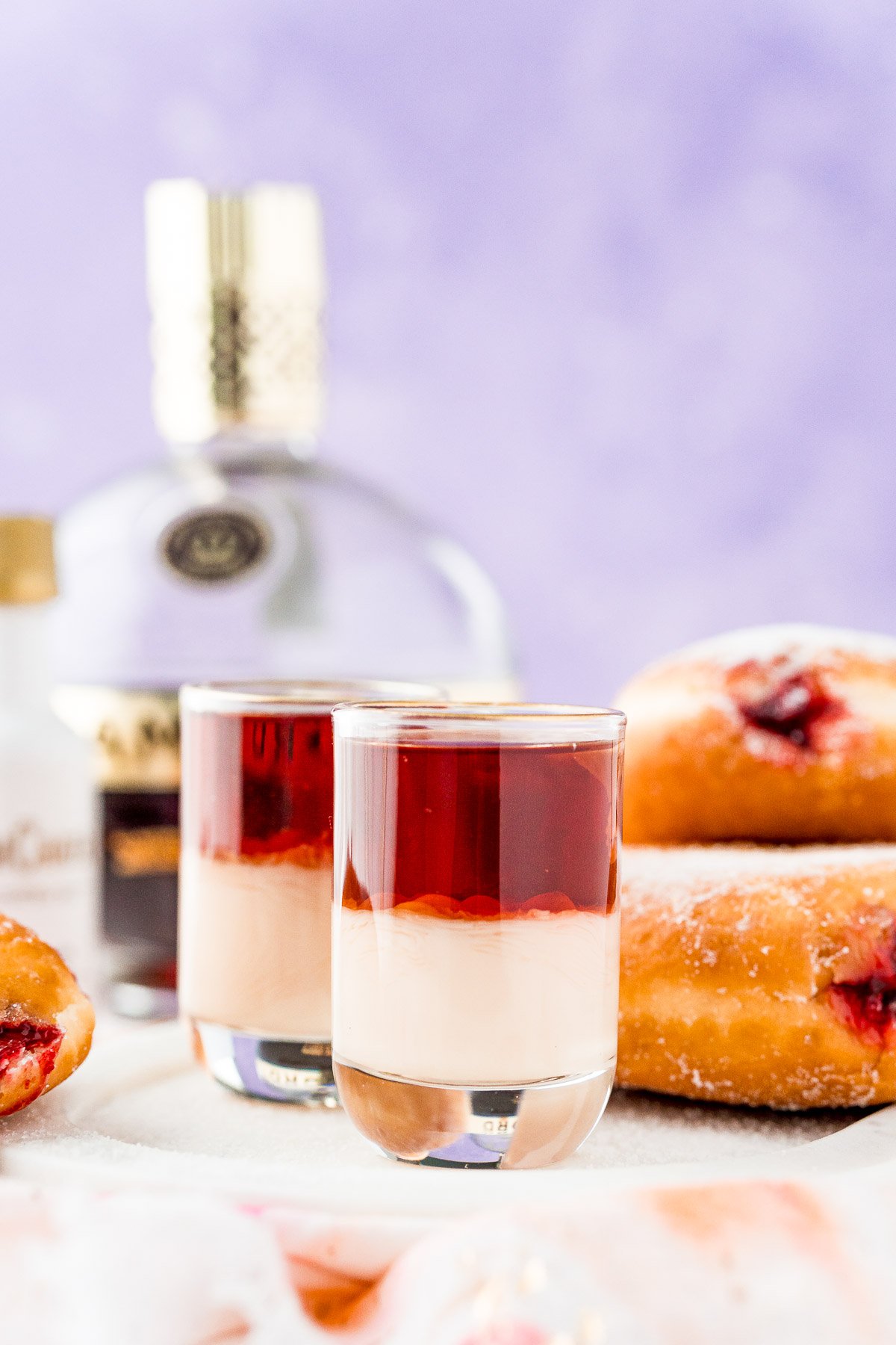 Jelly donut shots on white serving tray with donuts in the background.