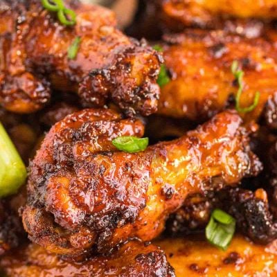 Close up photo of chicken wings coated in a sticky sauce and topped with scallions.