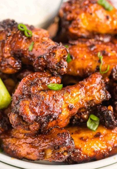 Close up photo of chicken wings coated in a sticky sauce and topped with scallions.