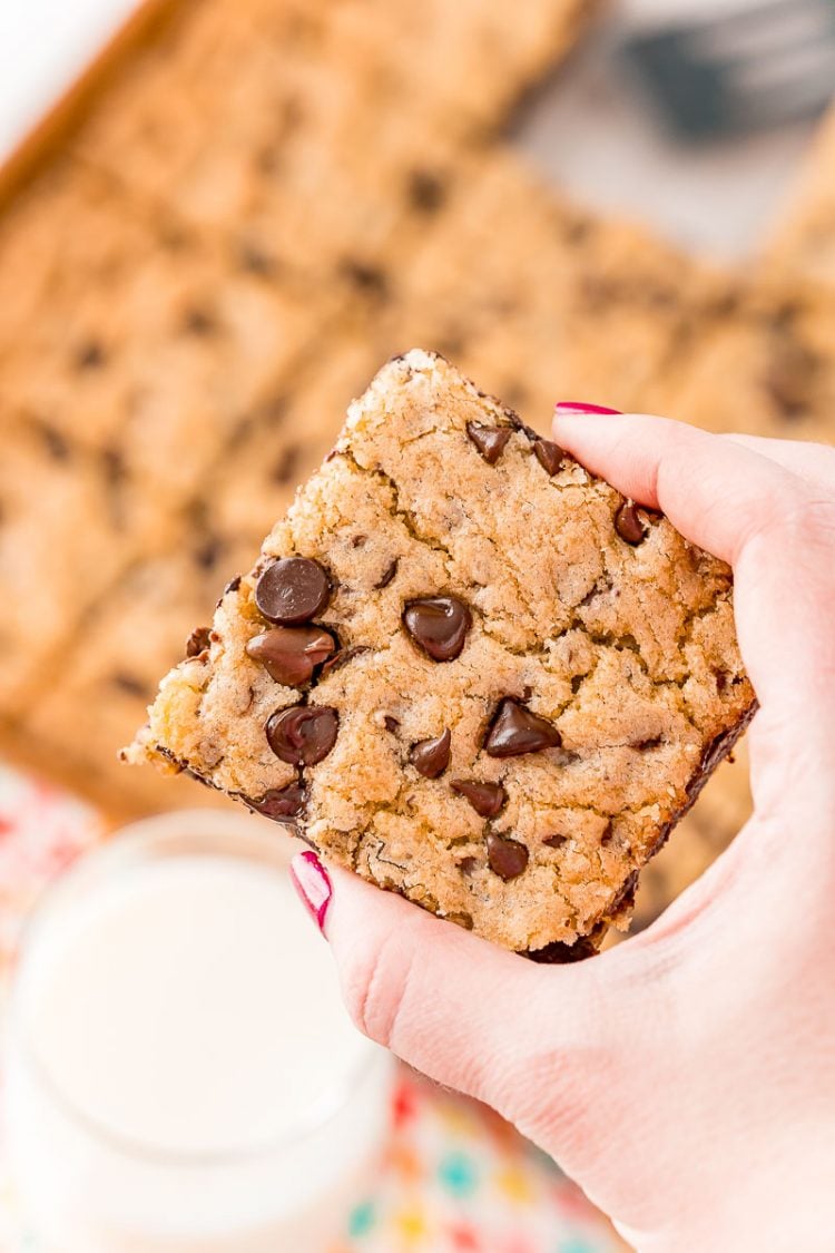 Woman's hand holding a chocolate chip cookie square.