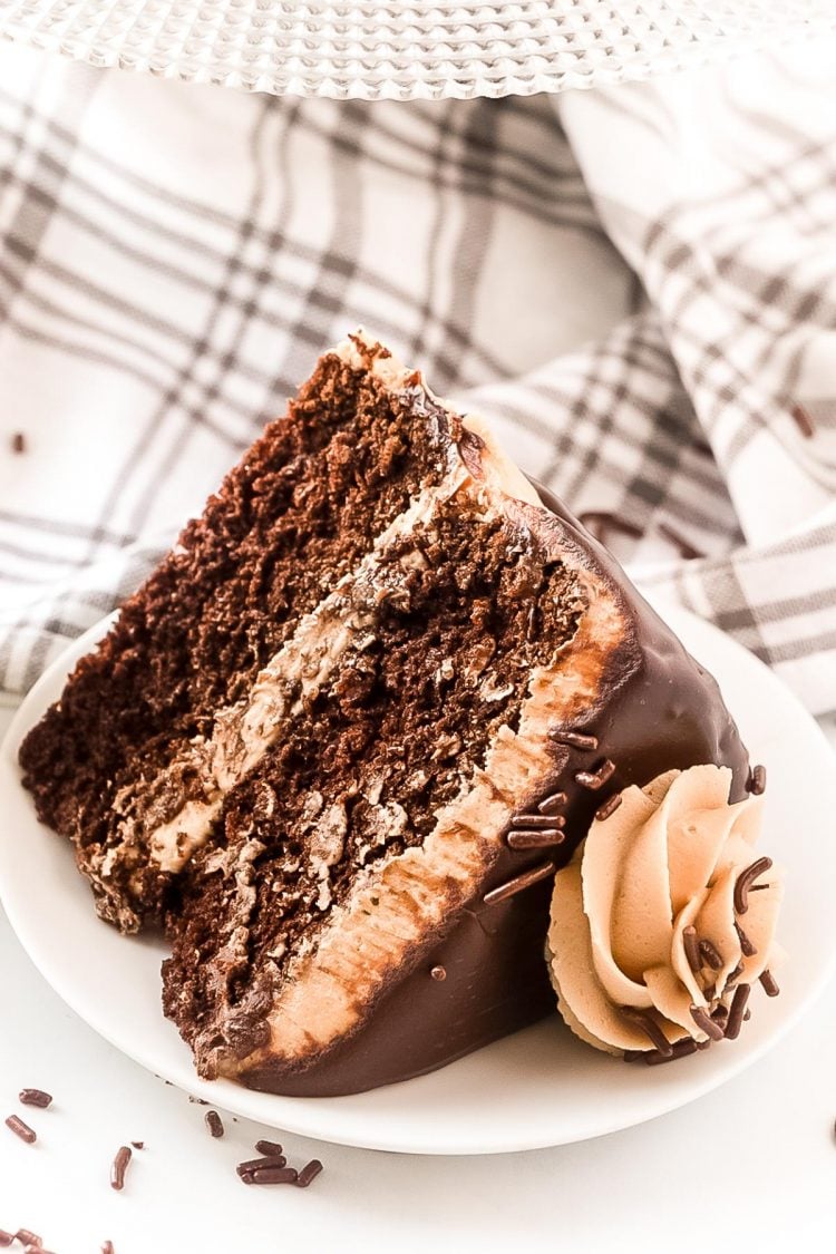 A slice of chocolate cake with cookie butter frosting laying on a white plate.