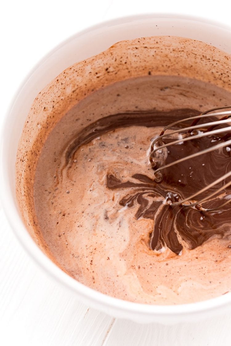 Chocolate and cream being whisked into ganache in a white bowl.