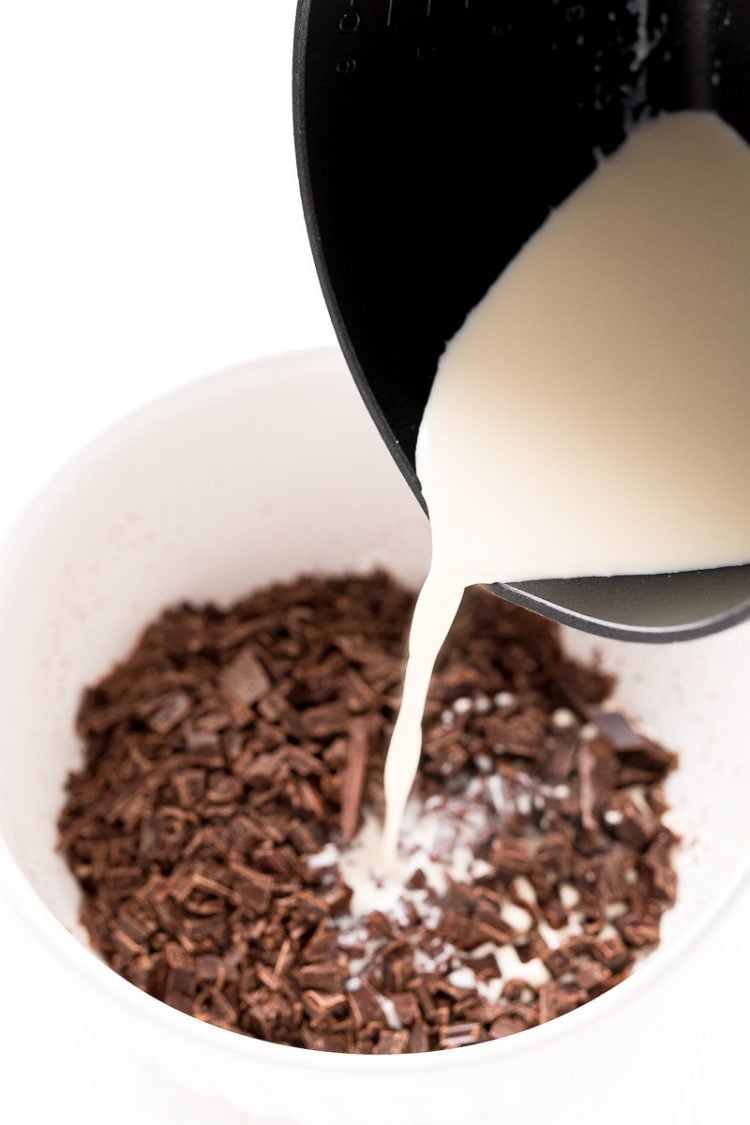 Cream being poured from a saucepan into a bowl of chopped chocolate