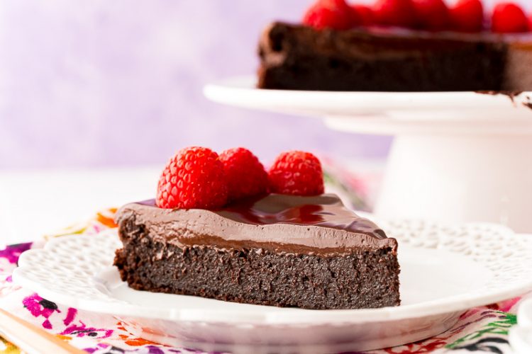 Slice of chocolate cake topped with raspberries on a white plate.