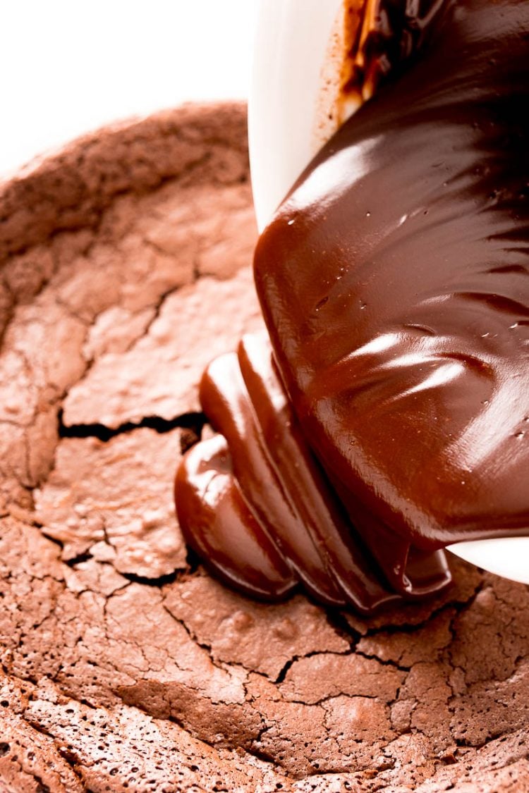 Chocolate ganache being pouring over the top of a chocolate cake.