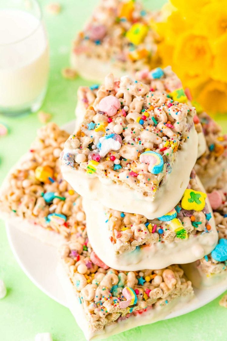 Lucky Charms Treats arranged on a white plate with a glass of milk and daffodils in the background.