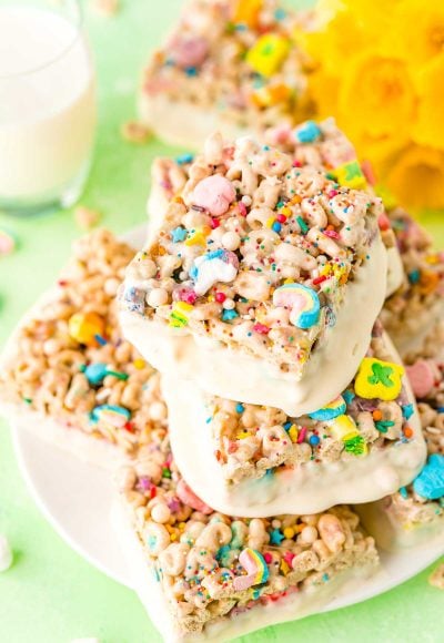 Lucky Charms Treats arranged on a white plate with a glass of milk and daffodils in the background.