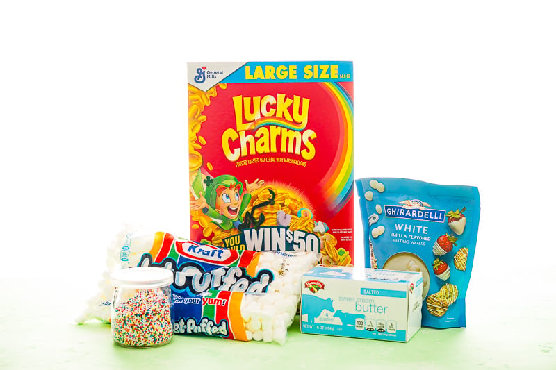 Photo of ingredients to make lucky charms treats including sprinkles, marshmallows, lucky charms cereal, butter, and white chocolate.