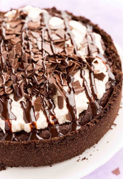 Close up photo of a Mississippi Mud Pie on a white cake stand with chocolate pieces and chocolate drizzle on top.